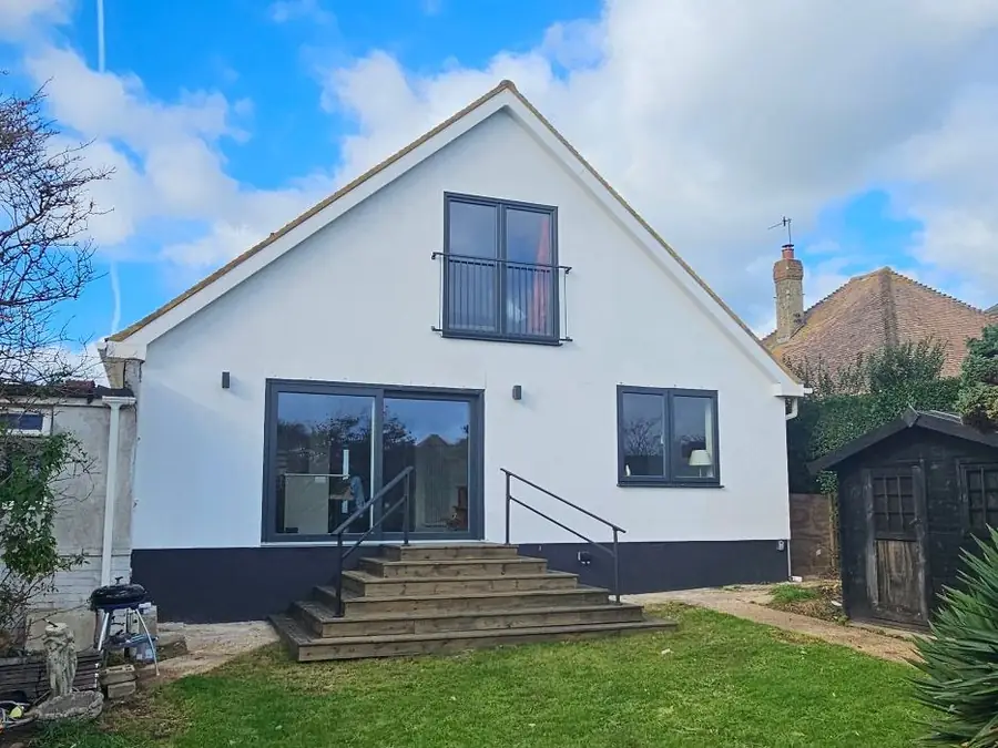 The finished house from the garden: white render, a gable window, large glazed doors and timber steps